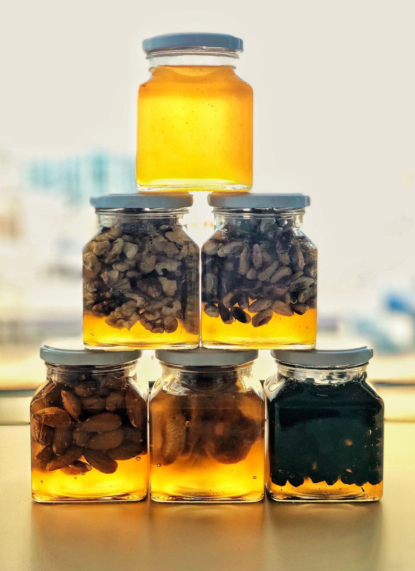 Artistic arrangement of honey jars with nuts and seeds against a light backdrop, creating a warm glow.