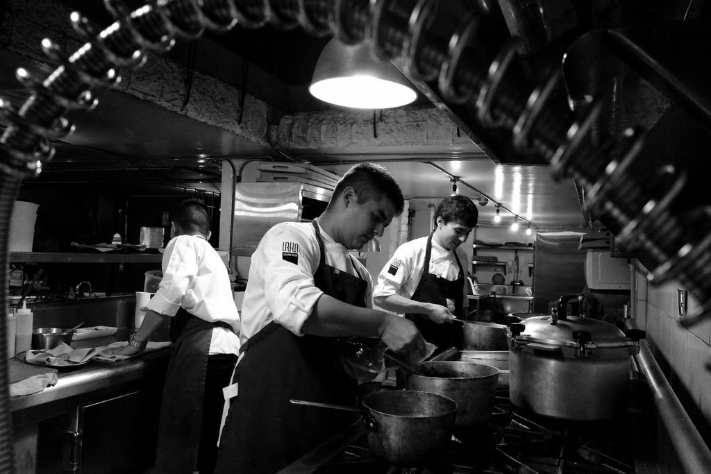 Black and white image of chefs preparing meals in an industrial restaurant kitchen.