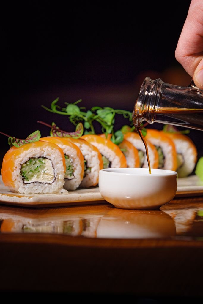 Close-up shot of delicious sushi rolls with soy sauce pouring into a dish, featuring vibrant colors.
