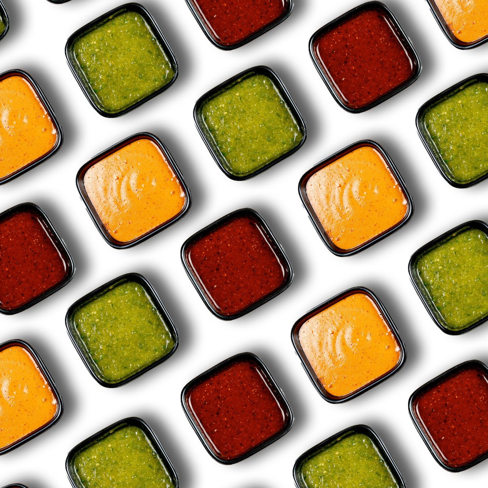 Top view of colorful sauces in square dishes, arranged neatly on a white background.