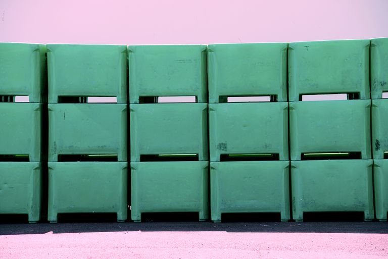 Row of green plastic tubs stacked against a pink wall. Industrial and storage concepts.