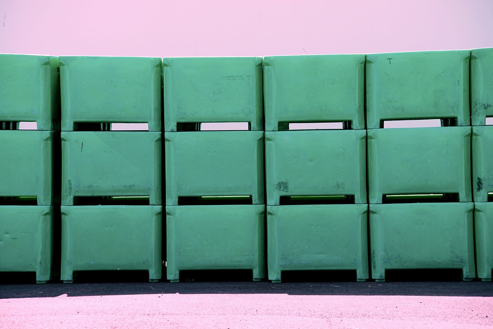 Row of green plastic tubs stacked against a pink wall. Industrial and storage concepts.
